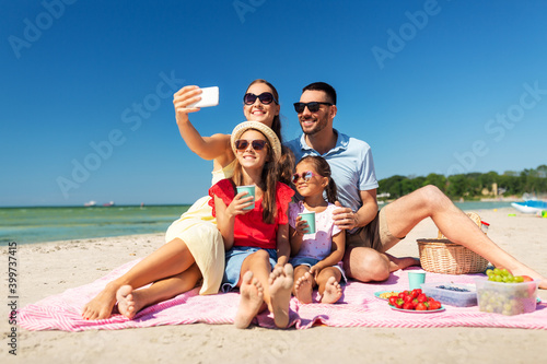 family, leisure and people concept - father, mother and two little daughters taking selfie with smartphone on summer beach