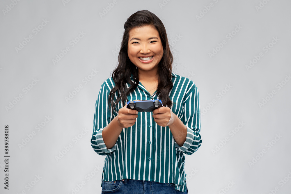 people, leisure and gaming concept - happy asian young woman playing video game with gamepad over grey background people, leisure and gaming concept - happy asian young woman playing video game with gamepad over grey background
