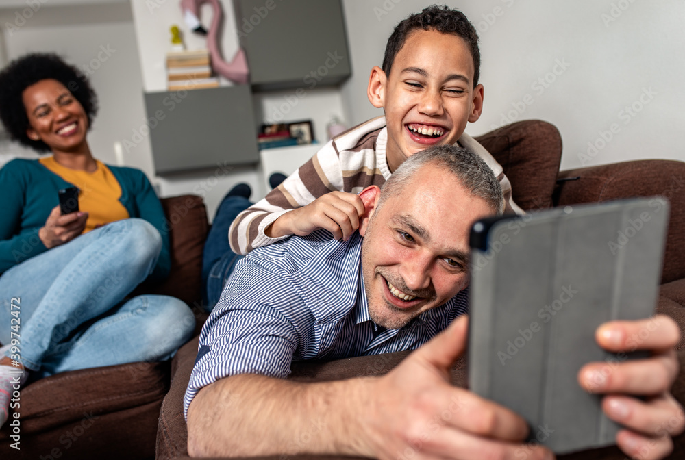 Smiling mixed race family enjoying time at home laying on sofa in living room making selfie with tablet. Smiling mixed race family enjoying time at home laying on sofa in living room making selfie with tablet.