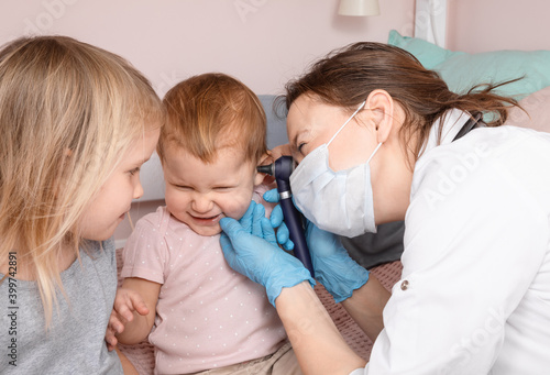 Pediatrician checking ear of baby girl with otoscope performing ENT exam at home during lockdown