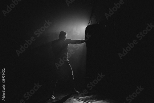 Fighter striking a blow. Professional sport. Fighting. Strength. Fighter in a moody light and grain mood. 
boxer training with punching bag in dark sports hall