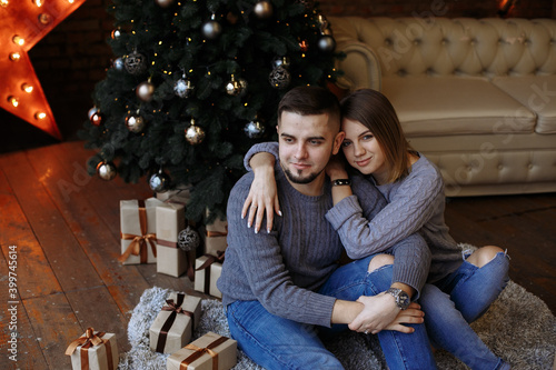 lovers are sitting under a christmas tree with gifts © Andrii