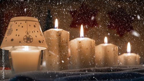 Candle lamp with multiple blured burning candles and snowing background on christmas atmosphere