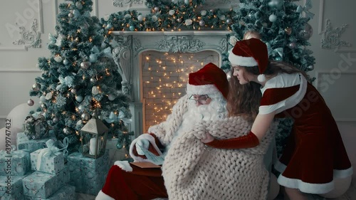 Santa Claus and his granddaughter read a letter. The girl covers Santa with a blanket.