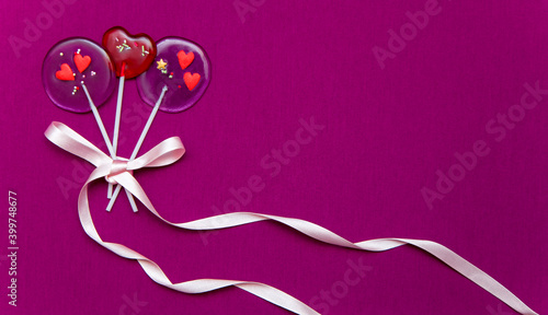 Lollipop hearts on a stick with ribbons on a pink background
