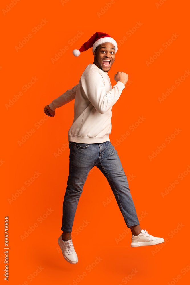 Cheerful Christmas. Funny Black Guy In Santa Hat Jumping In Air Cheerful Christmas. Funny Black Guy In Santa Hat Jumping In Air