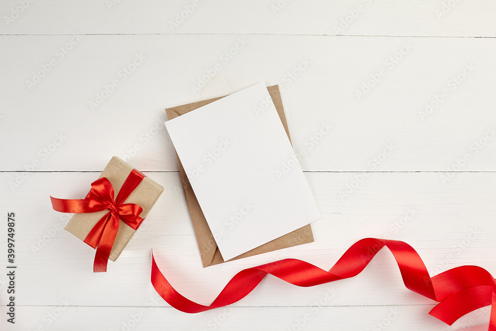 Greeting card mockup with paper envelope and red ribbon and gift box on white table Greeting card mockup with paper envelope and red ribbon and gift box on white table