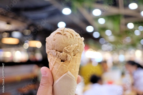 In selective focus a female hand holding a soft cone of coffee ice cream with blurred the mall area and dark background 