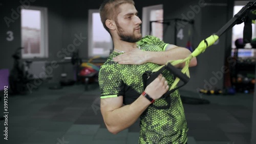 Strong sportsman training with TRX ropes during dynamic functional workout in modern gym 