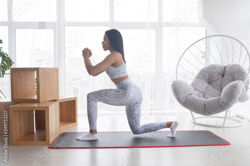 Sports during quarantine. Attractive black woman doing fitness on sports mat at home. Beautiful African American lady strengthening her body.
