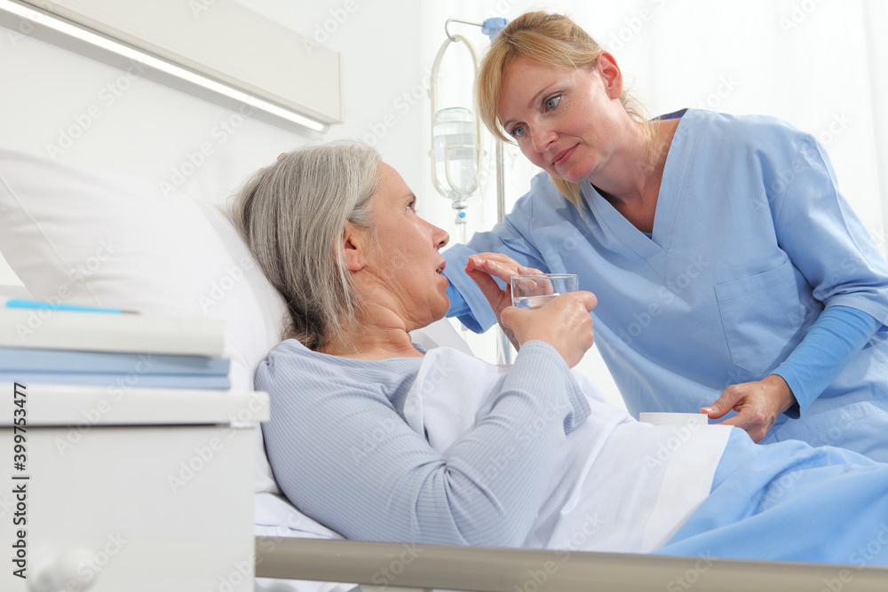Fototapeta premium nurse gives the pill to the elderly woman patient lying in the hospital room bed, concept of loneliness and old age diseases