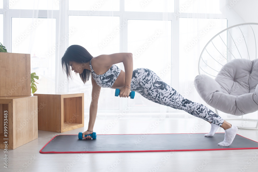 Indoor sports concept. Strong young black woman working out with dumbbells at home.