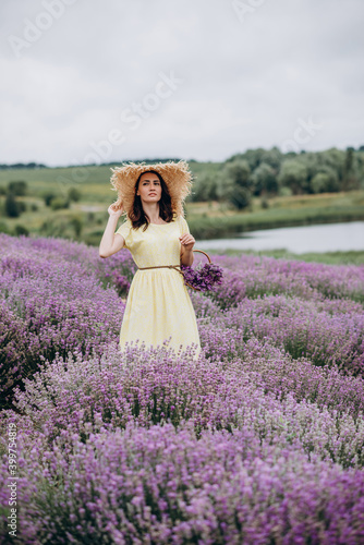 Beautiful woman in a yellow dress and hat with a basket of flowers in a field of fragrant lavender. Soft selective focus, art noise