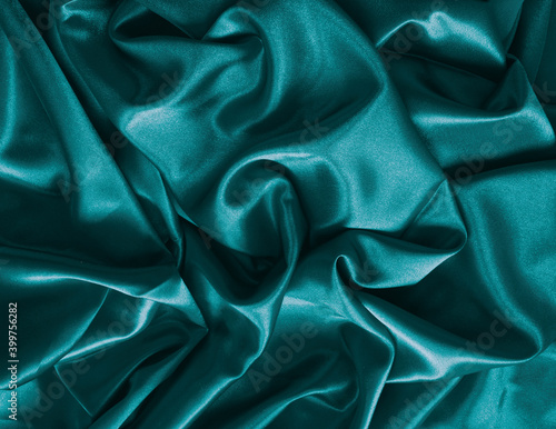 Elegant smooth blue green satin, silk fabric drapes. Luxurious cloth textile with liquid wave. Abstract background or template. Fabric shiny glitter texture. Luxurious blue background. 