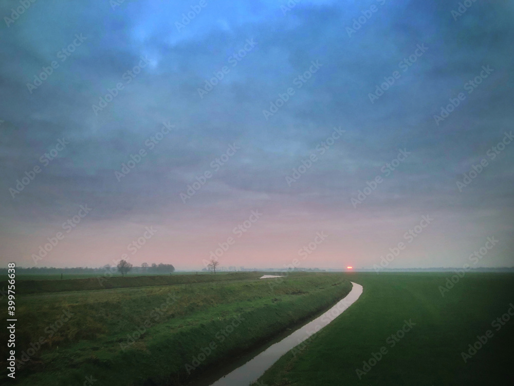 Misty sunset. Polder Netherlands. Havelte Drenthe. Ditch. Flat landscape and meadows. Evening. Winter.