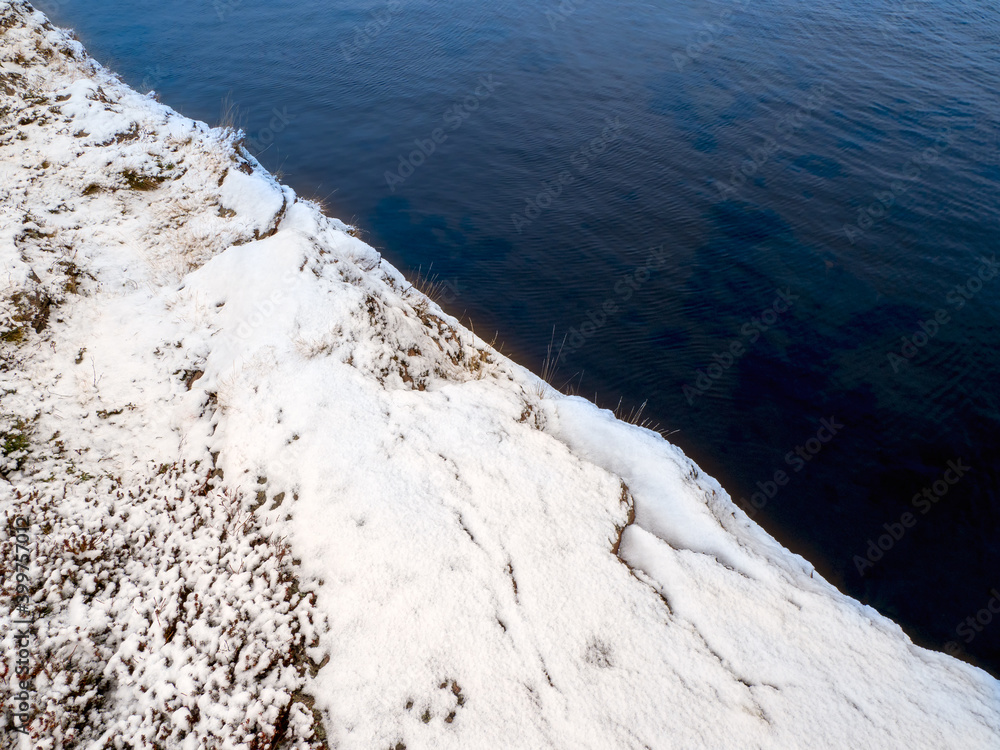 Cliff above the water, snow slope. Diagonal arrangement