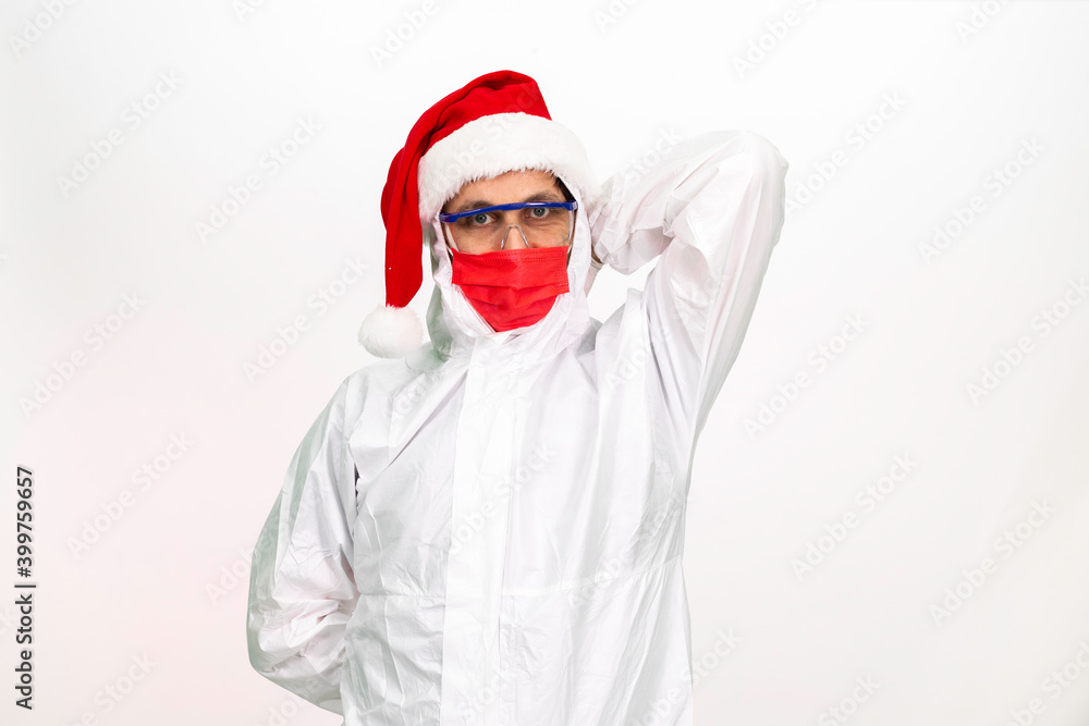 Health worker wearing protective clothing. He wears a santa hat on his head. He has a red corona mask on his face. Health worker wearing protective clothing. He wears a santa hat on his head. He has a red corona mask on his face.