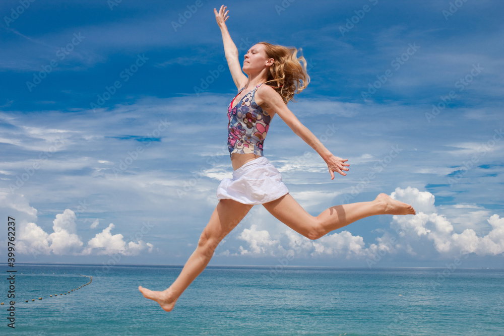 Happy girl twenty years old in summer clothes jumping on the beach against the background of the sea