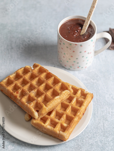 Two homemade waffles with a cup of hot chocolate over a white table.