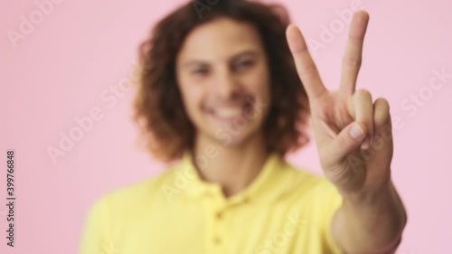 Wallpaper Mural A close-up view of a positive curly young man is showing peace gesture standing isolated over a pink background in the studio Torontodigital.ca