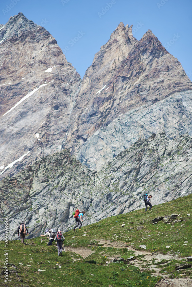 Beautiful view of large pyramidal peaks with hikers team. Male mountaineers walking uphill while hiking in mountains. Concept of travelling, hiking and mountaineering in Alps.