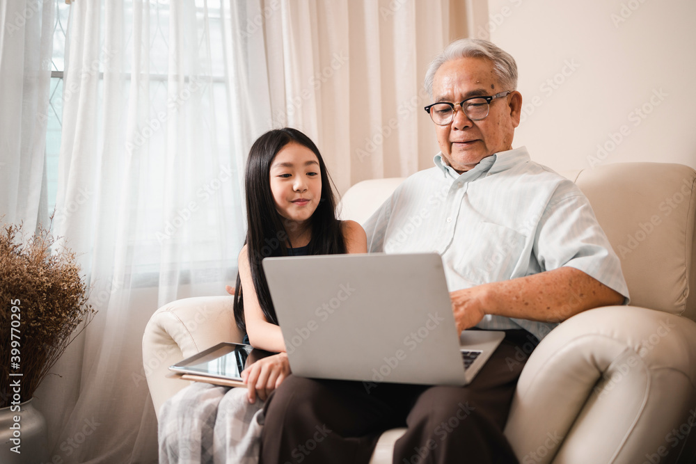 Happy Asian retirement grandfather and pretty granddaughter watching e-book for learning to education together by laptop. Happy Family educational at home concept. Technology and education.
