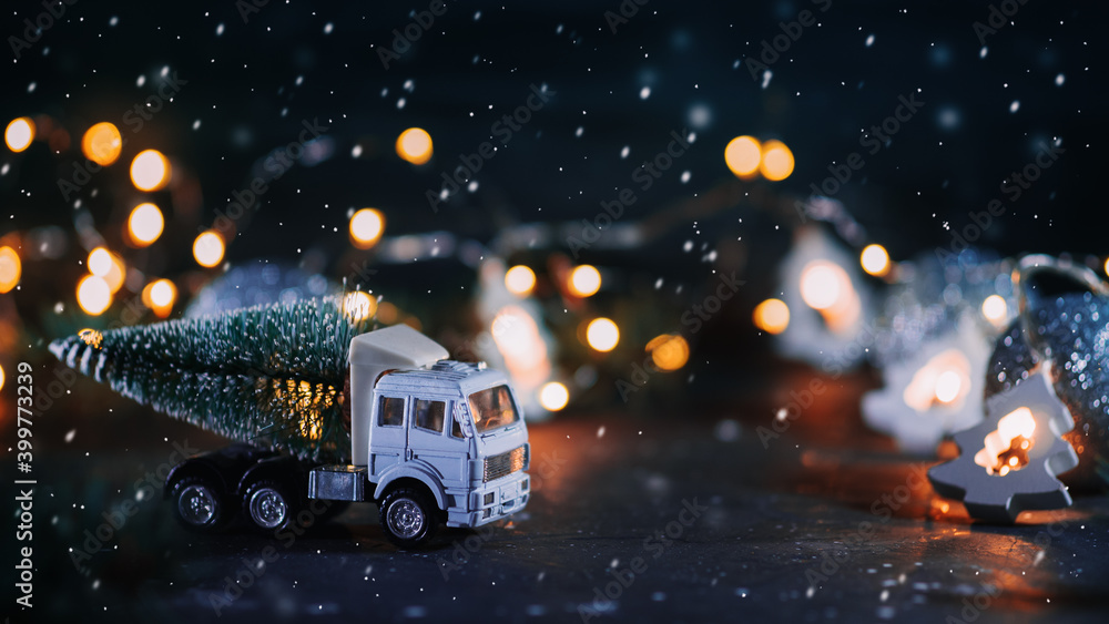 Toy truck with a Christmas tree on a dark background . christmas background, falling snow, light from garlands Toy truck with a Christmas tree on a dark background . christmas background, falling snow, light from garlands