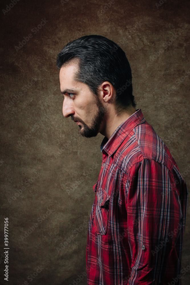 Male portrait in profile. man in a red shirt. Portrait on a brown background.