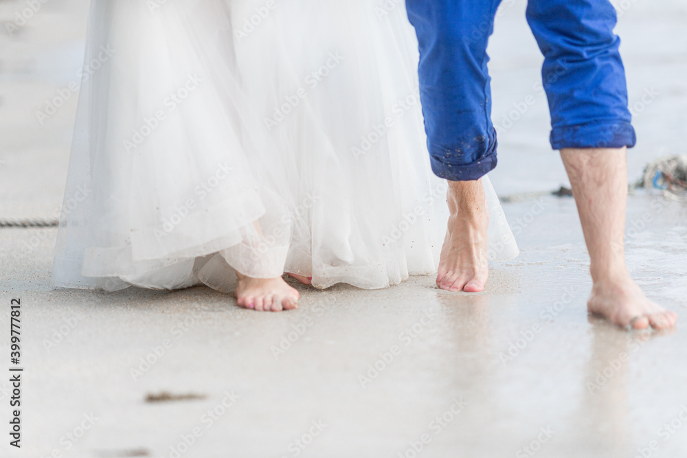 Legs of the bride and groom in a wedding dress walk along the sea beach