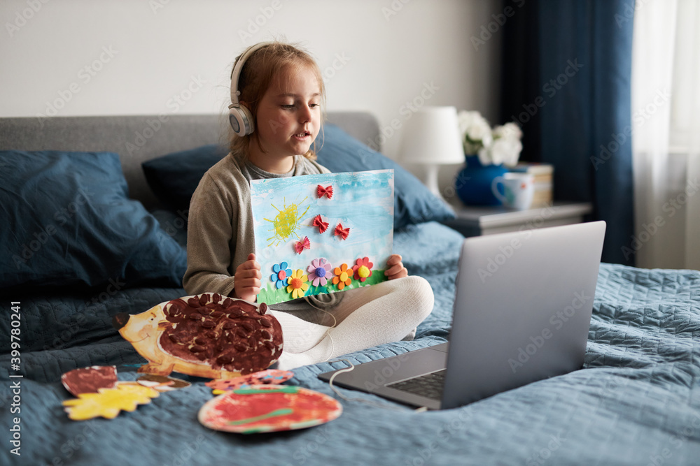 Little girl preschooler learning online showing her works drawings done at home. Child learning watching lesson remotely, talking with tutoress on video call from home during quarantine. Kid using lap