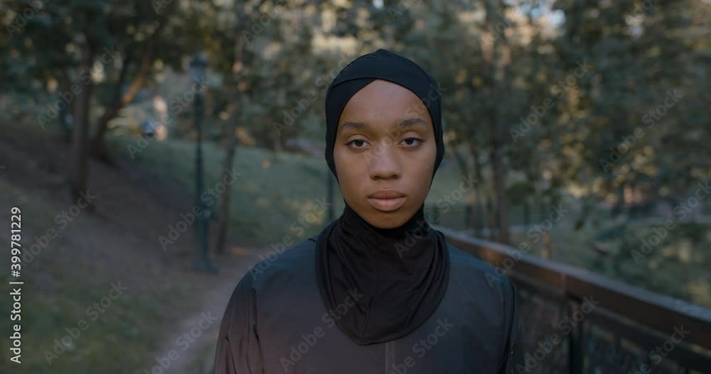Portrait of beautiful muslim woman turning head and looking to camera. Close up of afro american female person in hijab smiling while standing in park. Concept of lifestyle. Outdoors Portrait of beautiful muslim woman turning head and looking to camera. Close up of afro american female person in hijab smiling while standing in park. Concept of lifestyle. Outdoors