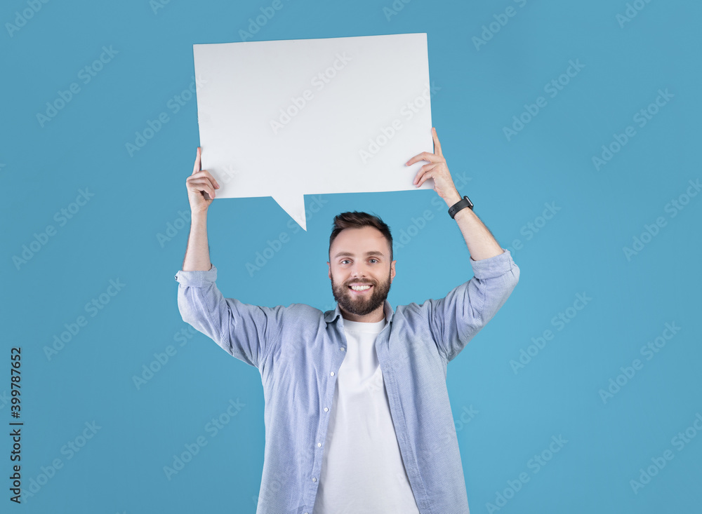 Happy millennial man holding blank speech bubble above his head over blue studio background, copy space Happy millennial man holding blank speech bubble above his head over blue studio background, copy space