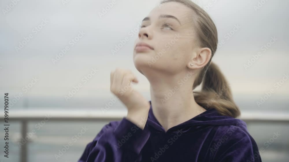 Close-up of confident beautiful sportswoman stretching neck at the background of cloudy overcast sky. Portrait of charming young Caucasian woman warming up before morning workout outdoors. Close-up of confident beautiful sportswoman stretching neck at the background of cloudy overcast sky. Portrait of charming young Caucasian woman warming up before morning workout outdoors.
