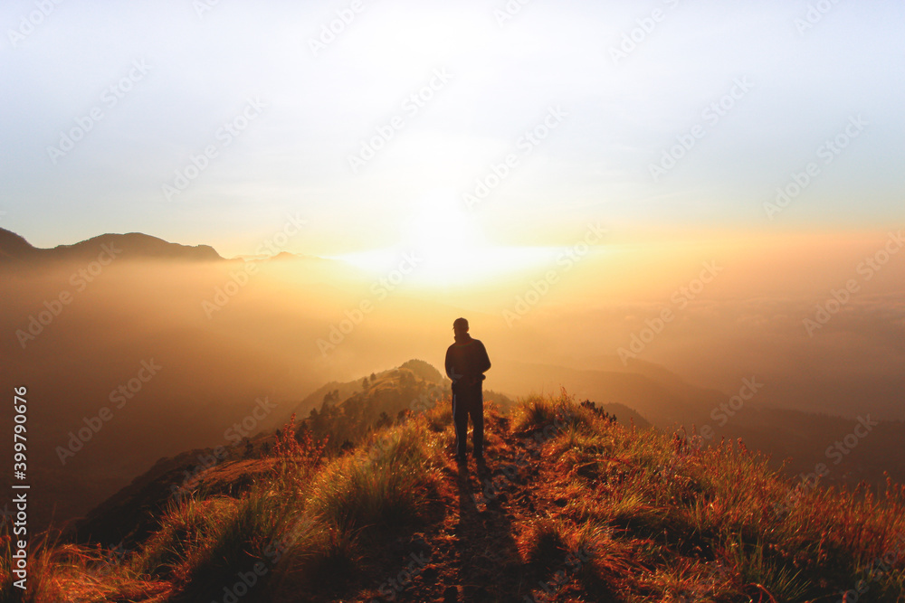 Man enjoying beautiful cloudscape sunrise on top of mountain cliff. Asian man in meadow misty fog background.