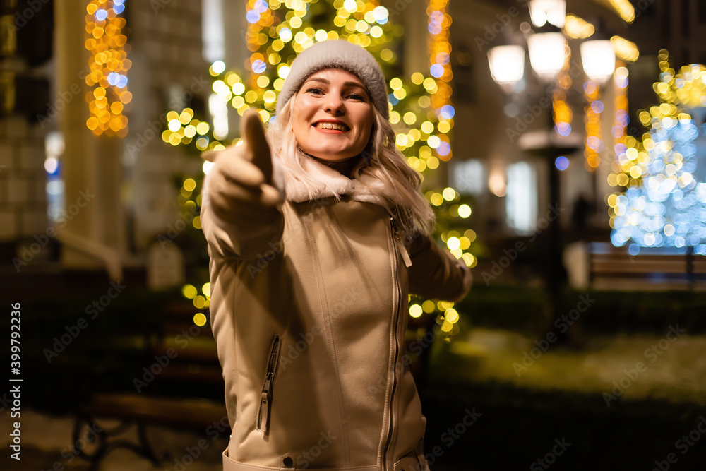 Street portrait of smiling beautiful young woman on the festive Christmas fair. Lady wearing classic stylish winter knitted clothes.