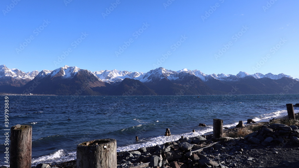 Old abandoned dock pilings along the shore with Kenai Mountains and Resurrection Bay in background on a cold winter morning in Seward Alaska
