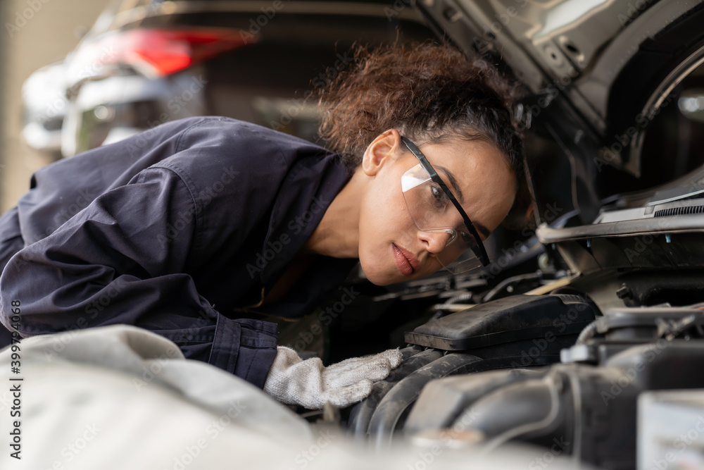 Female mechanic working at the garage. Professional female car mechanic examining, repair and maintenance under hood of car at auto car repair service. Car service and Maintenance concept Female mechanic working at the garage. Professional female car mechanic examining, repair and maintenance under hood of car at auto car repair service. Car service and Maintenance concept