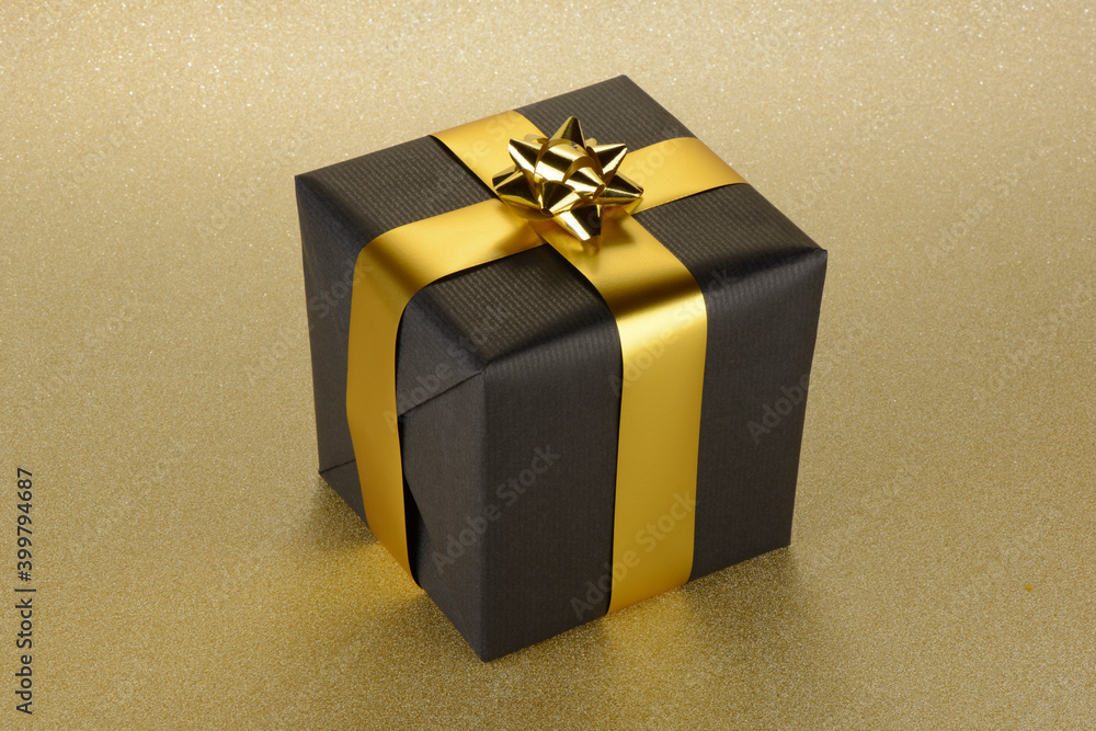 Caja regalo negra y dorado sobre fondo de brillantina dorada en forma de cubo Photo | Adobe