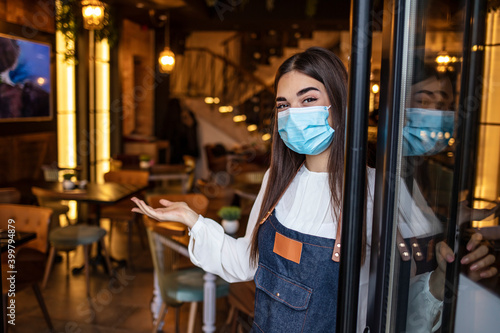 Woman wearing mask standing with open sign board on glass door in coffee shop and restaurant after coronavirus lockdown quarantine.Business crisis concept.