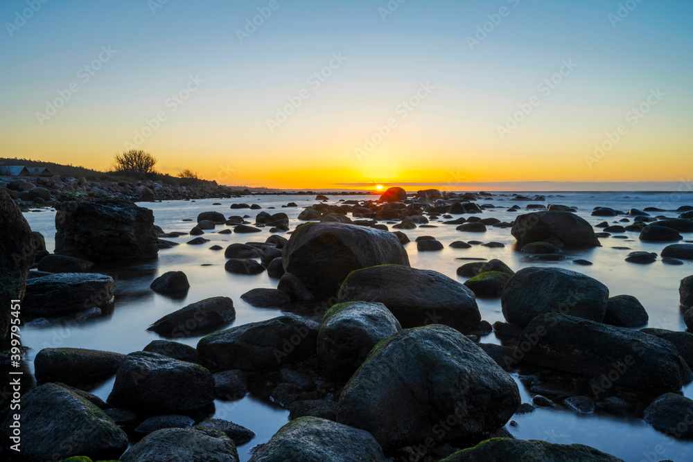 Boulders laying in shallow water with an cold winter sunset in the background, at the island of Gotland in Sweden Boulders laying in shallow water with an cold winter sunset in the background, at the island of Gotland in Sweden