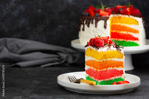 Canvas Print Rainbow slice of cake with fresh berries on dark background.