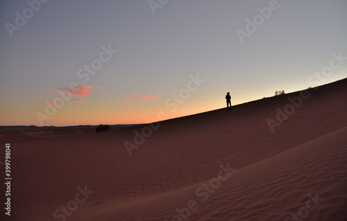 Eine Silhouette einer Person auf einer Sanddüne in der Wüste im Abendlicht