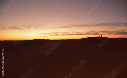 Dämmerung in der Sahara mit Menschen, die auf Sandbergen sitzen und das Naturschauspiel beobachten