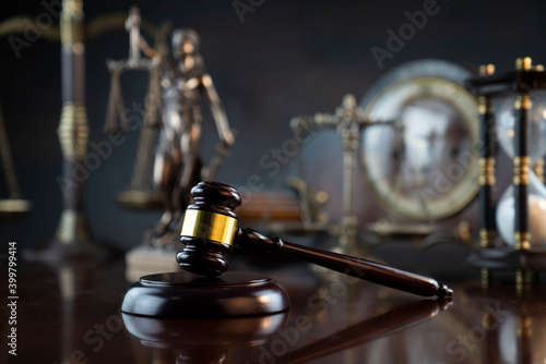 Law symbols composition. Judge’s gavel, Themis statue, scale, hourglass and old clock on the shining wooden brown table and the gray background.