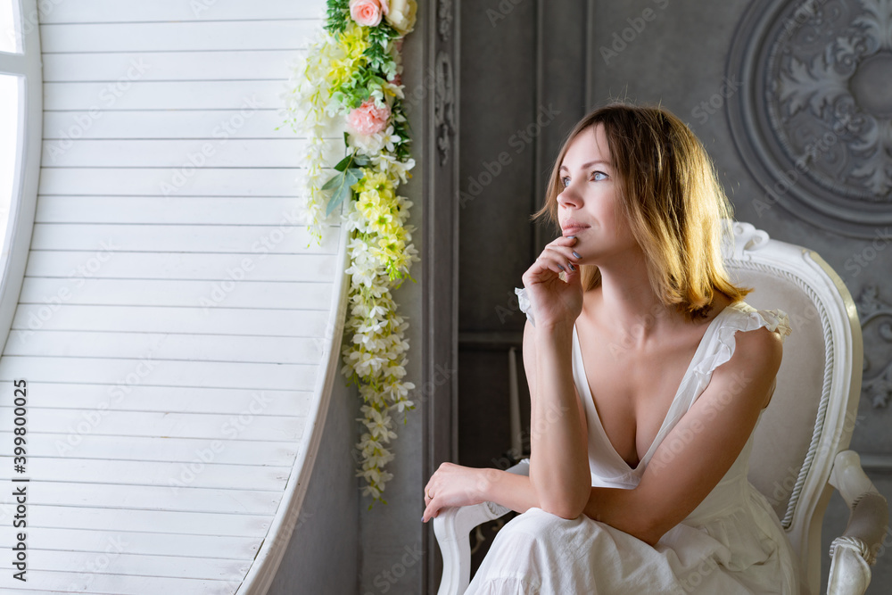 Fototapeta premium A woman in a white dress indoors looks to the side at the light.