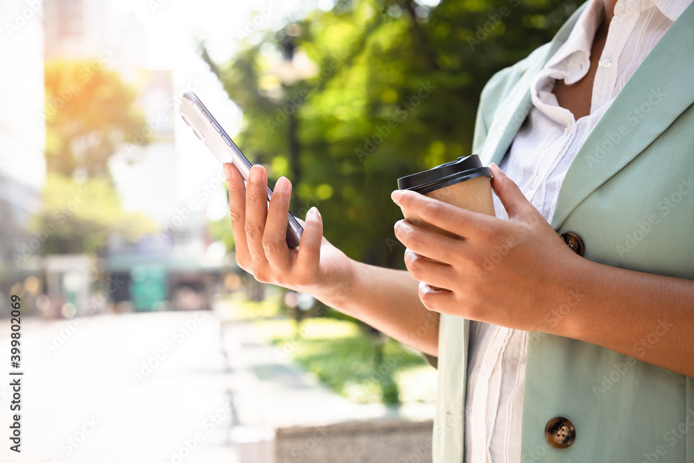Close-up image of young businesswoman walking with smartphone at sunny city streets and drinking coffee to go outside, She wearing casual suit style.