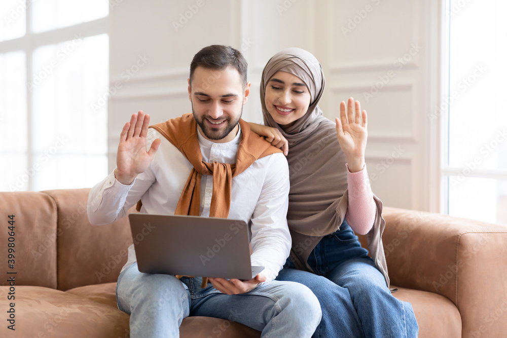 Muslim Couple Making Video Call Using Laptop Sitting At Home Muslim Couple Making Video Call Using Laptop Sitting At Home