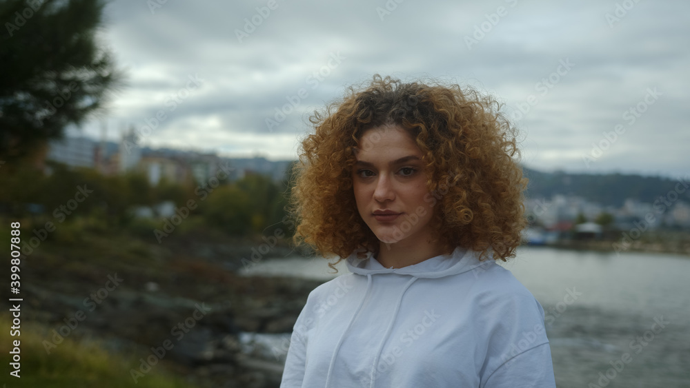 Portrait of smiling young woman in white sportswear with curly hair. Park, sea background Portrait of smiling young woman in white sportswear with curly hair. Park, sea background
