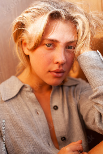 soft portrait of beautiful young blonde woman without make-up in gray linen shirt in wooden interior with sunlight