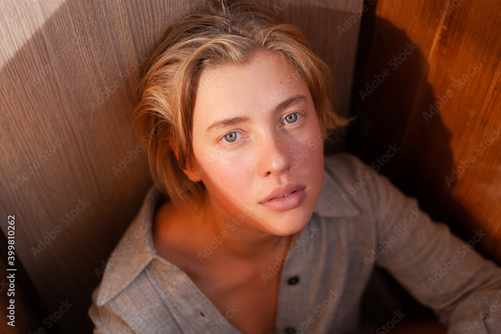 soft portrait of beautiful young blonde woman without make-up in gray linen shirt in wooden interior with sunlight soft portrait of beautiful young blonde woman without make-up in gray linen shirt in wooden interior with sunlight